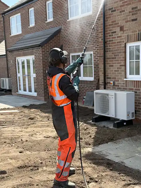 Roundhouse UK technician in high-visibility PPE pressure washing brickwork on a new-build home at a construction site.