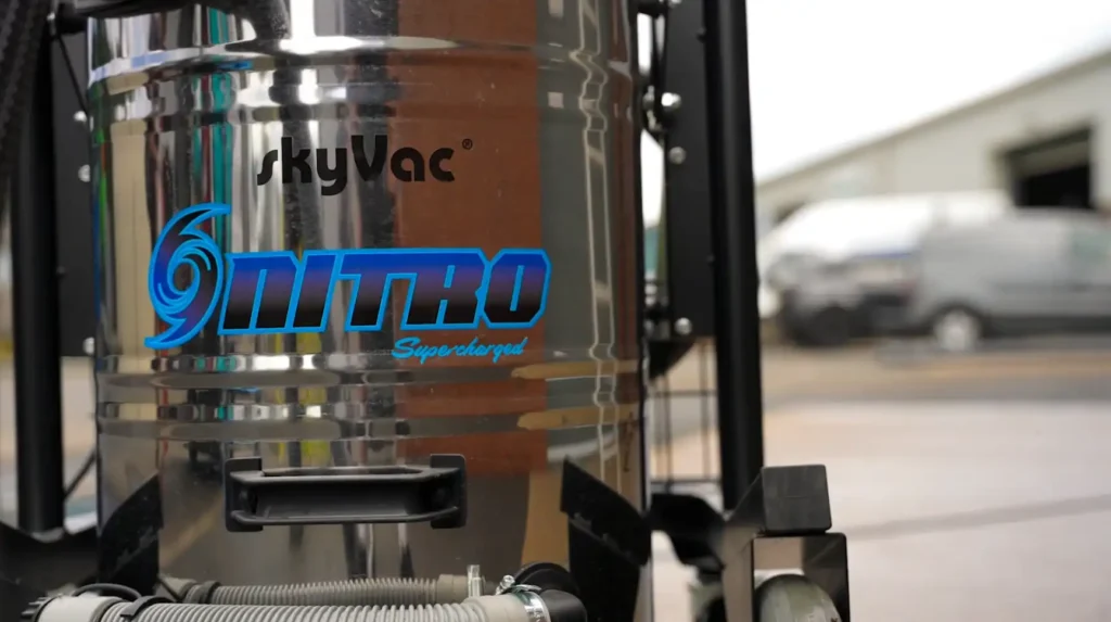 Close-up of a polished SkyVac Nitro stainless-steel drum vacuum on wheels, showing blue “Nitro” branding outside a warehouse.