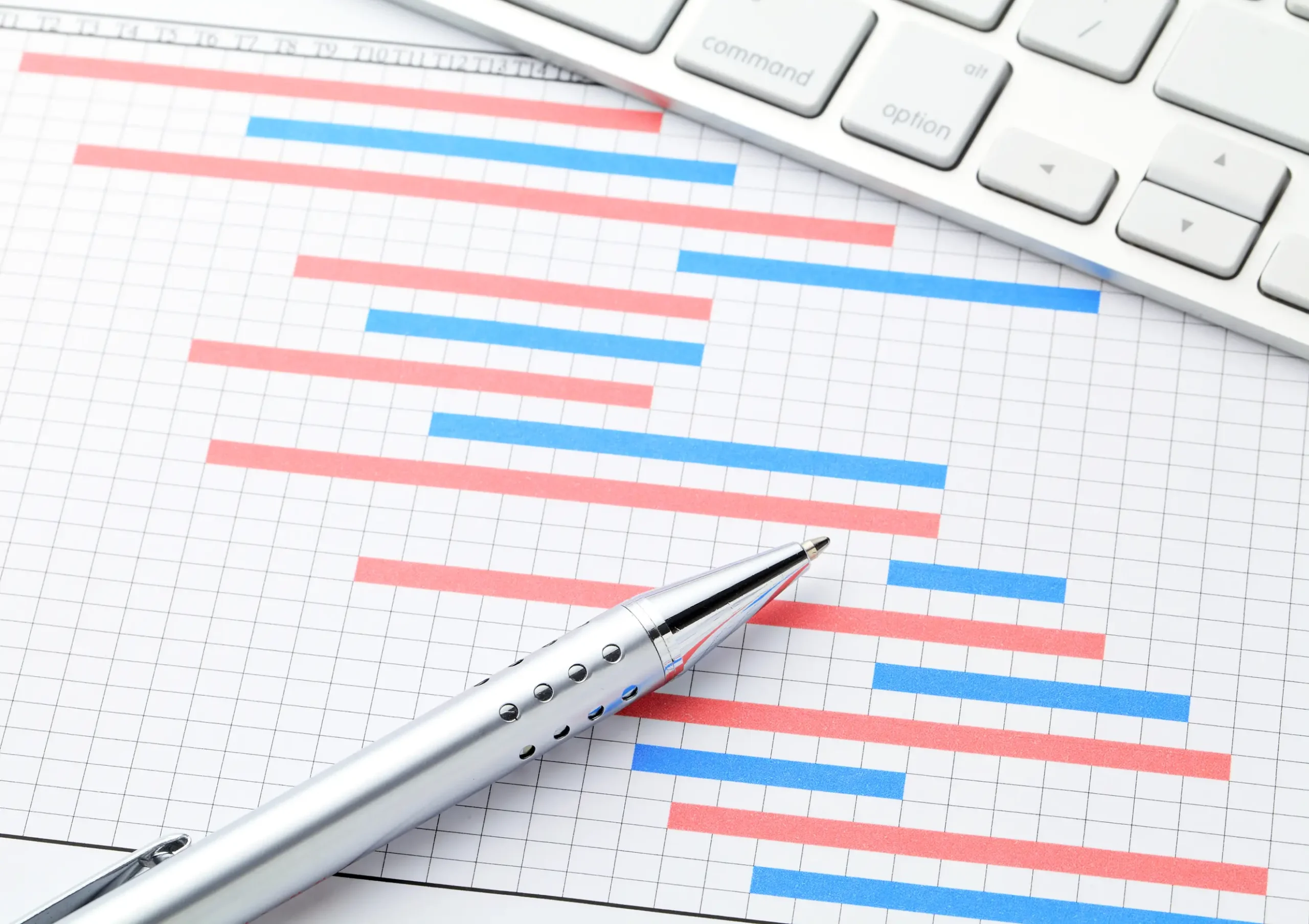 Close-up of a Gantt chart with a silver pen and computer keyboard, representing technology-driven planned preventative maintenance scheduling.