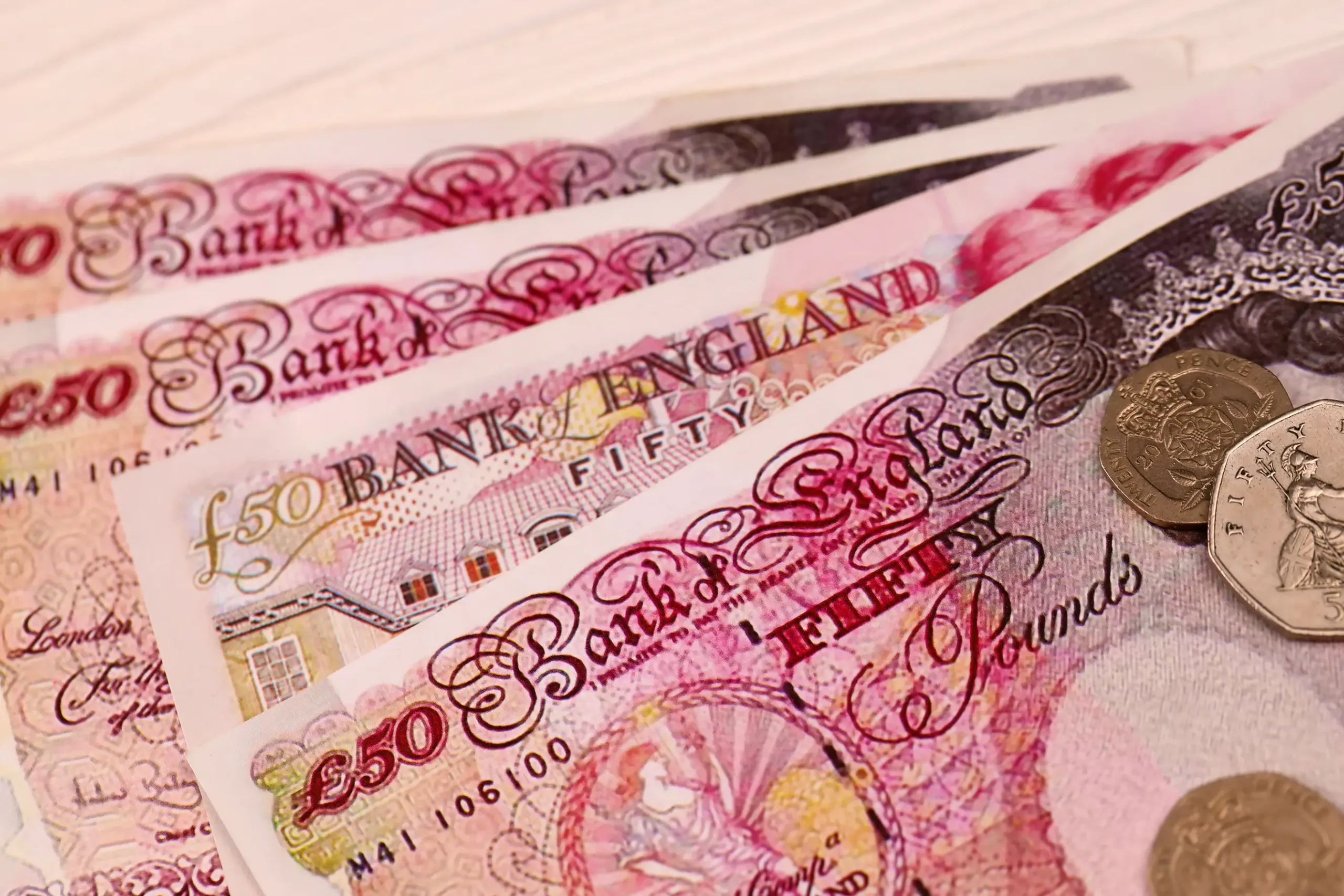 Close-up of UK £50 banknotes and coins symbolising the high costs of reactive maintenance.